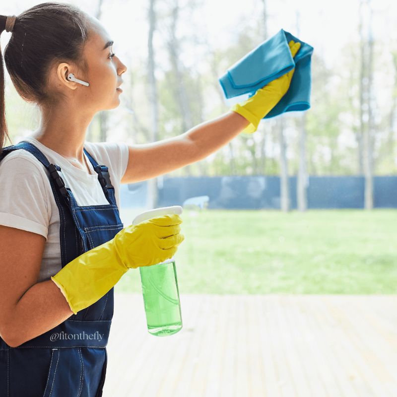 Young woman cleaning windows with gloves, an example of activities of daily living that boost fitness