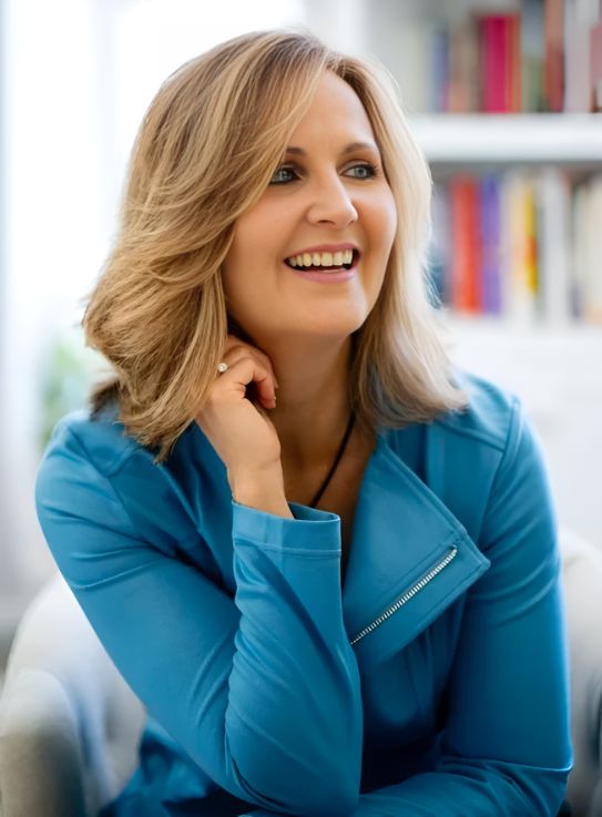 Smiling woman in blue jacket, sitting indoors.